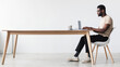 © Prostock-studio - A young black man is sitting at a desk in his home office, using a laptop for work or study. He is focused, with a coffee cup nearby, in a minimalist environment.