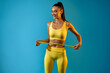 © Prostock-studio - A cheerful fit woman wearing a yellow outfit measures her waist with a tape measure. She looks happy after achieving her weight loss goal, standing in front of a blue studio background.