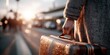 © keks20034 - A traveler holds the handle of a suitcase against the backdrop of the airport in the warm morning light