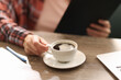 © New Africa - Coffee break. Woman with cup of aromatic drink and clipboard at wooden desk indoors, closeup
