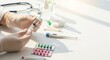 © Dara - A doctor's hands holding a syringe with a needle, surrounded by medical supplies and a stethoscope on a white table.