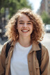 © Imagine  - Smiling young woman with curly hair wearing casual outfit and backpack standing outdoors in sunny urban street, representing confidence, happiness, freedom, and modern lifestyle in natural daylight