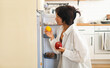 © Mykola - Back view of brunette woman standing in front of opened refrigerator full of food products, choosing ingredients to cook nutritious healthy breakfast before going to work