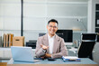 © laddawan - Confident Asian businessman standing with arms crossed in modern office, smiling with pride and success, representing leadership, ambition