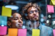 © ttonaorh - Group of young professionals collaborating during brainstorming session, using colorful sticky notes on glass wall in modern office.