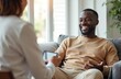 © Vadym - African man talks with therapist. Patient laughs during consultation in bright room. Doctor holds tablet. Focus on cheerful client during therapy session. Mental wellness, healthcare, assistance