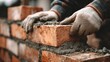 © Oleksandr - Close-up of bricklayer's hands carefully positioning a brick on a wall, showcasing construction precision and craftsmanship.  Focus on masonry, texture, and labor.