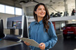 © Graphicroyalty - Confident female car sales agent in business attire holding a clipboard, standing beside a sleek new vehicle inside a bright dealership showroom.