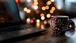 © Yuliia - Festive red mug with snowflake pattern next to laptop on wooden desk, with soft bokeh Christmas lights in background creating cozy holiday atmosphere.