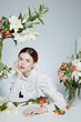 © SHOTPRIME STUDIO - Young woman in elegant white blouse surrounded by fresh flowers, exuding serenity and beauty in a soft pastel setting