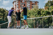 © qunica.com - Three friends celebrate a friendly tennis match on an outdoor court, giving high fives. Casual athletic wear and a sunny urban backdrop convey fitness, teamwork, and outdoor recreation.