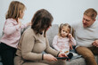 © qunica.com - A family seated together on a sofa, interacting and bonding. The image showcases familial love, togetherness, and the warmth of family connections in a home setting, emphasizing care and joy.