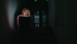 © qunica.com - A woman sits on a dark staircase in a dim hallway, focused on her laptop. The laptop screen casts a glow on her thoughtful face, conveying concentration, solitude, and late-night work.