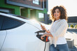 © Serhii - Happy woman charging electric car at home using smartphone app