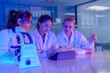 © ultramansk - A team of female researchers collaborates on a biotechnology project. They are analyzing assay results on a tablet while performing a titration in a modern R&D laboratory.