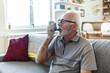 © Jelena Stanojkovic - Senior man using asthma inhaler for relief an attack at home. Mature man using medical inhaler to prevent and treat wheezing and shortness of breath caused by allergy.