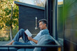 © we.bond.creations - Mature man reading on a modern patio sofa, enjoying peaceful solo time outdoors in sunlight and greenery, relaxed and thoughtful