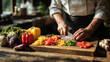 © Nobelus - Chef chopping colorful fresh vegetables including peppers, onions, and tomatoes on a wooden cutting board in a bright kitchen with natural light.