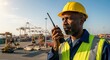 © Vasiliy - African American foreman using a walkie-talkie at a busy shipping port. Industrial worker coordinating logistics at a container terminal. Global trade and supply chain management