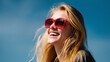 © Ольга Ничипорчук - ChatGPT ÑÐºÐ°Ð·Ð°Ð»:Close-up portrait of a joyful young woman with long blonde hair, laughing under bright summer sunlight, wearing stylish oversized red sunglasses. The blue sky in the