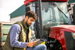 © Mediteraneo - Young tractor driver using tablet beside tractor