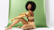 © Milan - Elegant Black woman with an afro hairstyle in gold satin lingerie and long gloves. Stylish model posing in a studio against a festive green glitter background.
