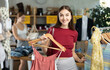 © JackF - In trading hall, girl choose and buy something summer clothing, choose some items. Discount season, promotional offers. Chain affordable clothing store. Female client choosing something in background