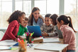 © Prostock-studio - Joyful school children engage with their teacher in a dynamic learning session at their desks. They explore study materials together in a bright, inviting classroom setting.
