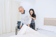 © Creativa Images - Caring Nurse or Granddaughter Assisting Elderly Man with Transfer from Wheelchair to Bed