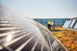 © Westend61 - Two technicians studying plan on the roof of a company building with solar panels