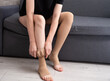 © Paulina_OK - Female model wearing compression socks sitting on grey sofa indoors demonstrating healthy lifestyle, vein care and prevention of venous disease