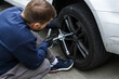 © Екатерина Лукашина - Young man unscrewing lug nuts on a car wheel with a wrench while replacing a flat tire on the road