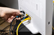 © Alina - Human hand plugging a black Ethernet cable into a white internet router, establishing a secure network connection for modern digital technology setup