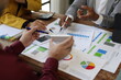 © Wasan - Business people analyzing financial charts and documents using calculator and laptop during a working meeting discussing company strategy and planning.