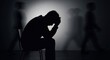 © Vasiliy - Silhouette of a depressed man sitting alone in a dark room. Blurry figures walk past, representing social isolation. Mental health, anxiety, and stress concept