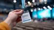 © perfectlab - Hand holding a conference badge with lanyard in a large auditorium with blurred audience and stage lights in the background
