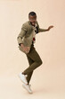 © TrueFrame Collective - Young Black man jumping with energetic pose against plain background, wearing glasses and smiling, body angled sideways, arms extended, expressing dynamic movement