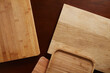 © ShapeImages - Overhead view of various wooden cutting boards and serving trays with different textures, including bamboo and natural wood grain, arranged randomly on a dark brown table surface.