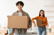 © Prostock-studio - In a bright, modern room, a young Asian man and his girlfriend are unpacking cardboard boxes. They are smiling and enjoying the process of setting up their new home.