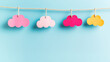 © Victoria - Brightly colored paper cut-out clouds in shades of pink, yellow, and red are hanging on a string against a clean light blue background, creating a playful and decorative scene with ample copy space