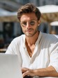 © Evgenia - Young professional freelancer working on laptop outdoors at a cafe, wearing sunglasses, with a relaxed atmosphere and natural light enhancing the creative workspace experience