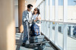 © bongkarn - Asian tourist couple go on trip man hugging talking woman while walking with luggage cart in airport