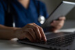 © bixpicture - Doctor in blue scrubs using laptop and tablet for telemedicine consultation, symbolizing digital healthcare, remote treatment, medical technology, and online patient communication system.