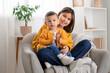 © Pixel-Shot - Teenage girl hugging her little brother with toy car in armchair at home