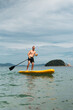 © Aboltin - Man balances on yellow paddle board in sea, focusing on stability and control. Summer water sport, strength, and concentration in nature. Falling off board with paddle.