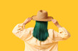 © Pixel-Shot - Young woman with green hair in hat on yellow background, back view