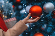 © Iryna - Person decorates a blue Christmas tree with red and silver ornaments during the holiday season at a festive outdoor market