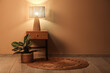 © Pixel-Shot - Wooden bedside table with glowing lamp and houseplant near beige wall in room