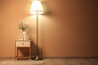© Pixel-Shot - White bedside table with beautiful flowers in vase and glowing floor lamp near beige wall in room