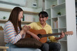© itchaznong - Joyful Music Session. A young couple laughing and enjoying a guitar performance in a cozy setting.
